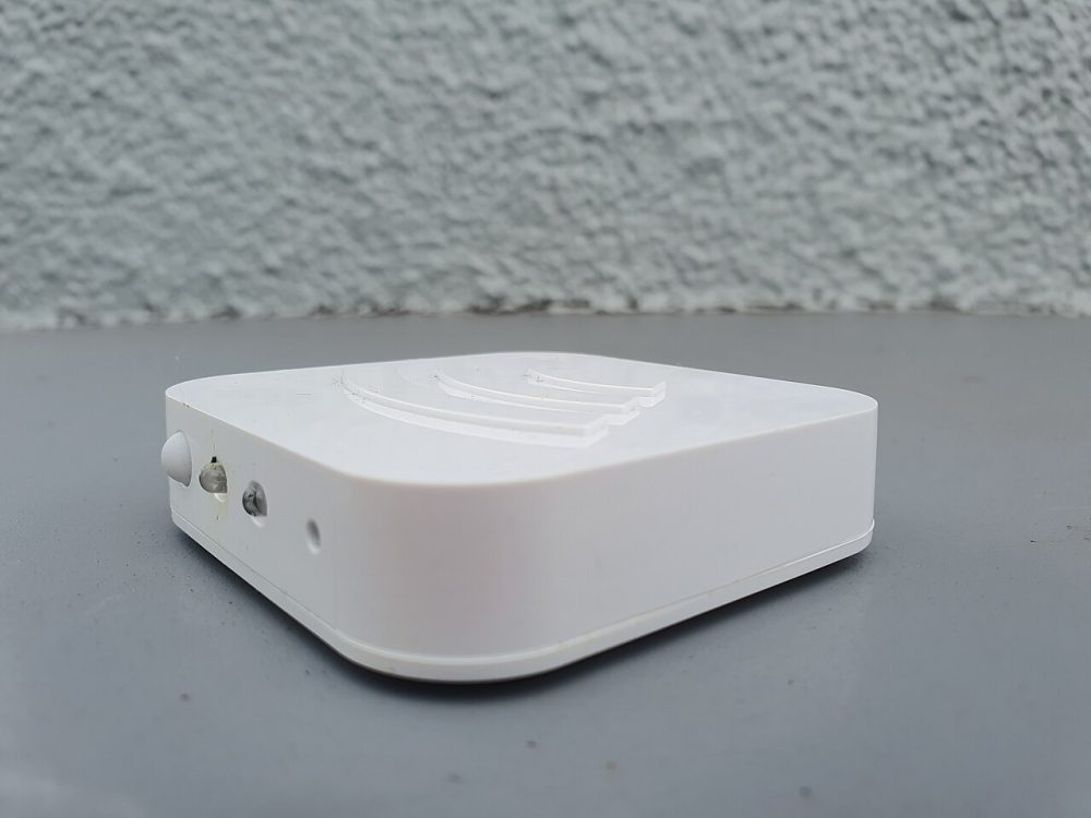 White rounded electronic device with an embossed wifi symbol on a grey surface against a textured blue wall.